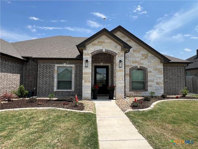 view of front of home featuring stone siding, a shingled roof, and a front yard