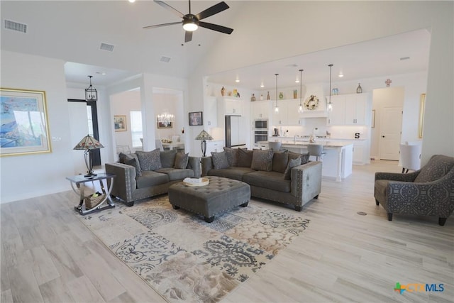 living room featuring high vaulted ceiling, ceiling fan with notable chandelier, visible vents, and light wood-type flooring