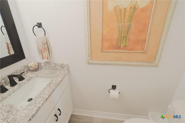 half bath featuring toilet, vanity, and baseboards