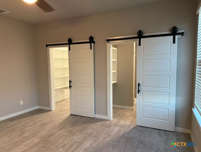 unfurnished bedroom with a barn door, a spacious closet, light hardwood / wood-style flooring, and ceiling fan