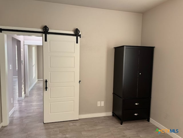 unfurnished bedroom with a barn door and light hardwood / wood-style flooring