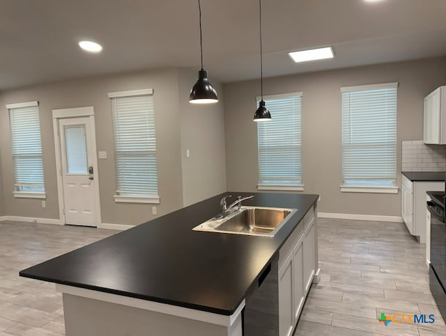 kitchen featuring pendant lighting, dishwasher, white cabinets, a center island with sink, and sink