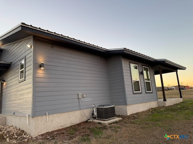 property exterior at dusk featuring a lawn and central AC