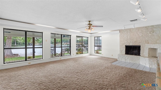 unfurnished living room with a ceiling fan, a textured ceiling, visible vents, a large fireplace, and carpet floors