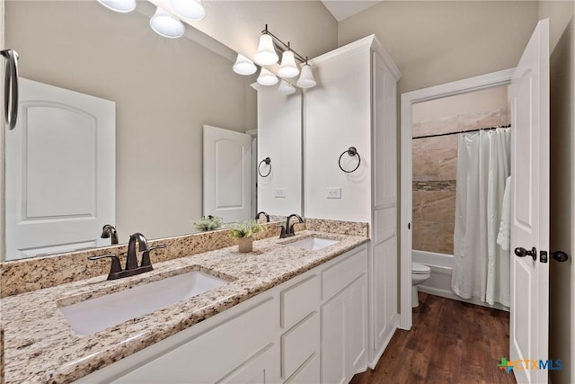 full bath with toilet, double vanity, a sink, and wood finished floors