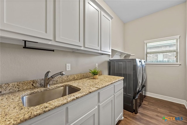 clothes washing area with washing machine and clothes dryer, cabinet space, a sink, wood finished floors, and baseboards