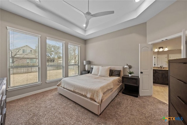 bedroom with light carpet, a ceiling fan, baseboards, a tray ceiling, and ensuite bath