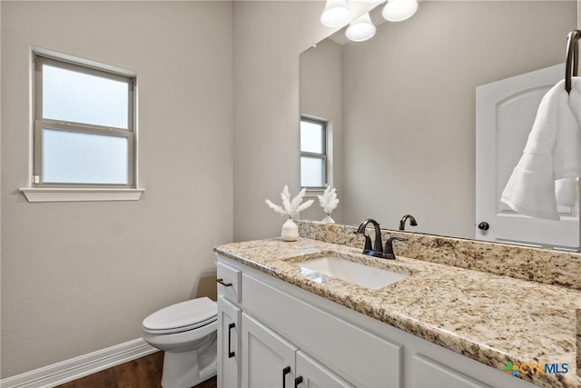 bathroom with baseboards, vanity, toilet, and a healthy amount of sunlight