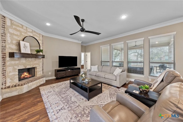 living area with ornamental molding, a ceiling fan, a brick fireplace, wood finished floors, and baseboards