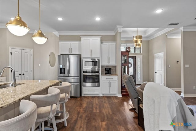 kitchen featuring dark wood-style flooring, crown molding, appliances with stainless steel finishes, white cabinets, and a sink