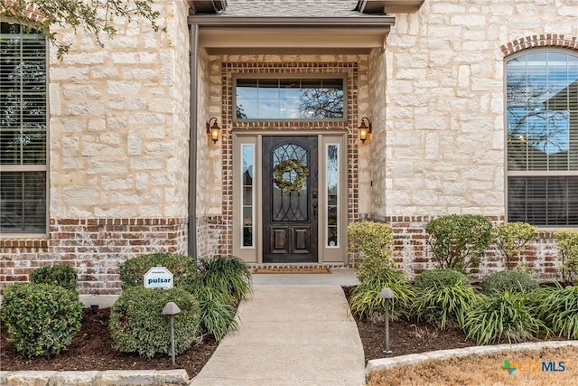 entrance to property with stone siding, brick siding, and roof with shingles