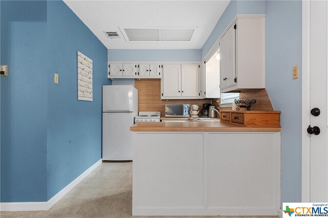 kitchen featuring light countertops, freestanding refrigerator, white cabinetry, a peninsula, and baseboards