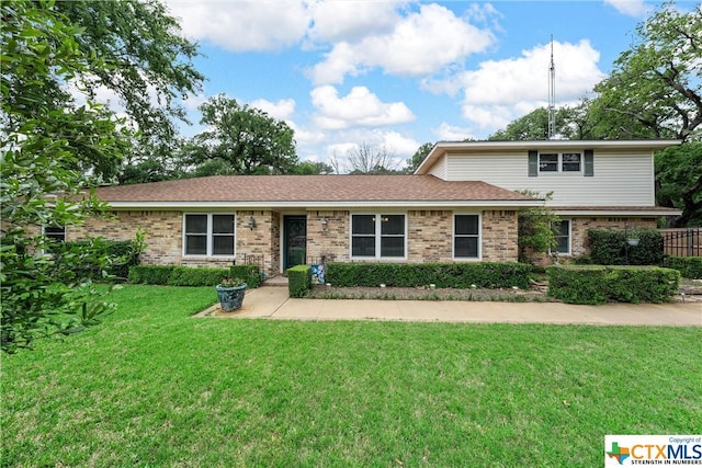 traditional-style home with a shingled roof, a front yard, and brick siding