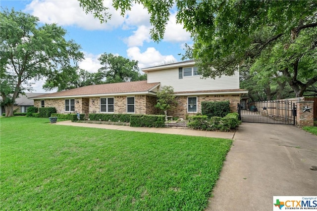 traditional-style house featuring a gate, brick siding, driveway, and a front lawn