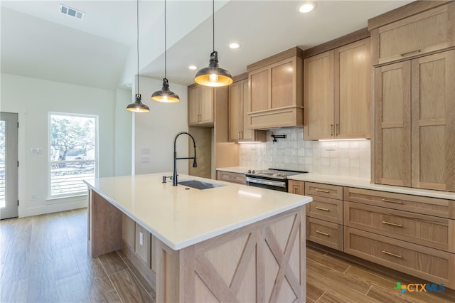 kitchen featuring stainless steel electric range, a center island with sink, light wood-type flooring, hanging light fixtures, and sink