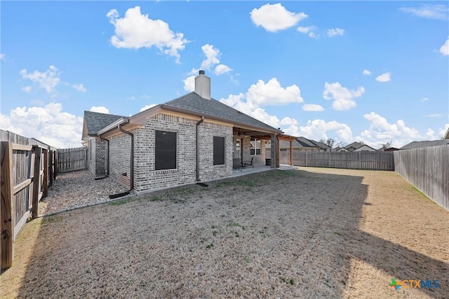 back of property with a fenced backyard, a chimney, roof with shingles, and brick siding