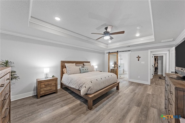 bedroom with a tray ceiling, crown molding, a barn door, light wood-style floors, and baseboards