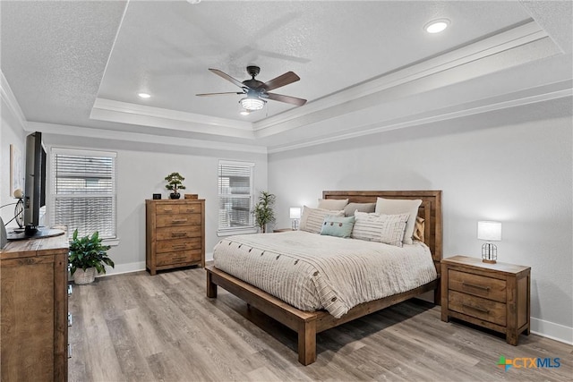 bedroom featuring light wood finished floors, a textured ceiling, a raised ceiling, and crown molding