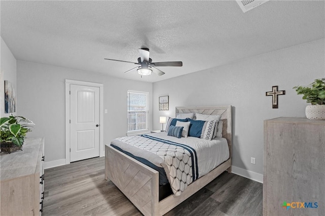 bedroom with baseboards, visible vents, a ceiling fan, wood finished floors, and a textured ceiling