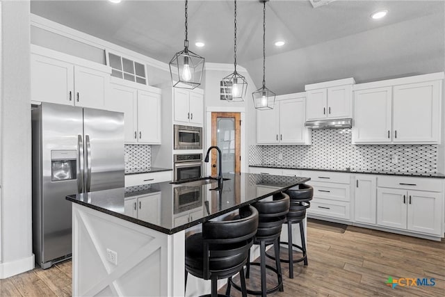 kitchen with white cabinets, a breakfast bar, a kitchen island with sink, stainless steel appliances, and a sink