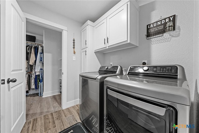 clothes washing area with a textured wall, wood finished floors, baseboards, washer and dryer, and cabinet space