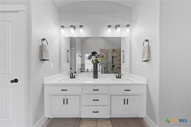 full bathroom featuring tiled shower, a sink, baseboards, and double vanity