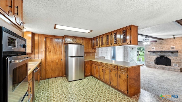 162 Lone Oak St, Seguin, TX 78155 - kitchen with stainless steel appliances, a peninsula, a fireplace, brown cabinets, and a textured ceiling