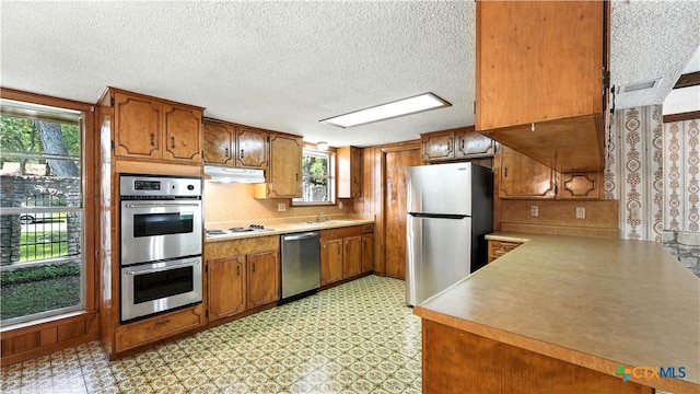 162 Lone Oak St, Seguin, TX 78155 - kitchen featuring stainless steel appliances, under cabinet range hood, brown cabinetry, light countertops, and a textured ceiling
