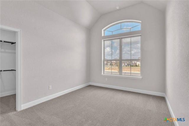 interior space with vaulted ceiling, a walk in closet, carpet flooring, and multiple windows