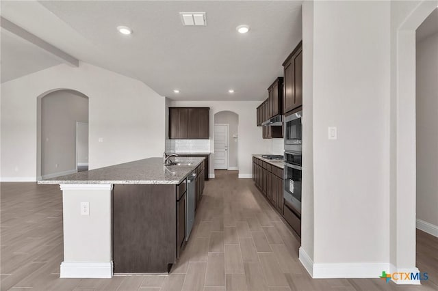 kitchen with a center island with sink, sink, vaulted ceiling with beams, light hardwood / wood-style floors, and stainless steel appliances