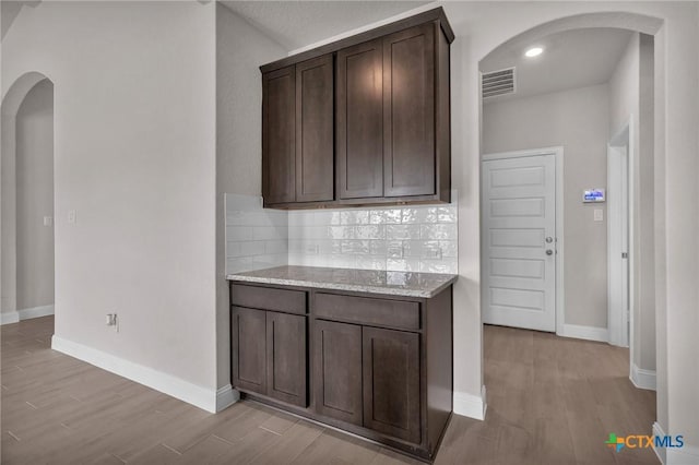 kitchen with light stone countertops, dark brown cabinetry, light hardwood / wood-style flooring, and backsplash