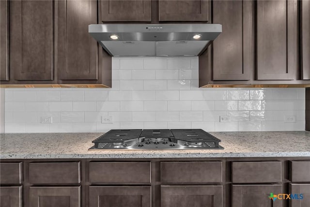 kitchen with decorative backsplash, dark brown cabinets, light stone countertops, and stainless steel gas cooktop