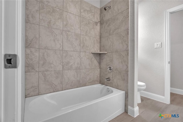 bathroom with hardwood / wood-style flooring, toilet, and tiled shower / bath