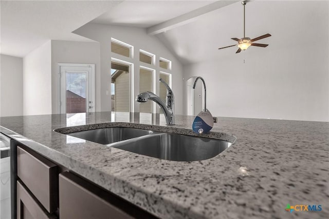 kitchen featuring lofted ceiling with beams, light stone counters, ceiling fan, and sink