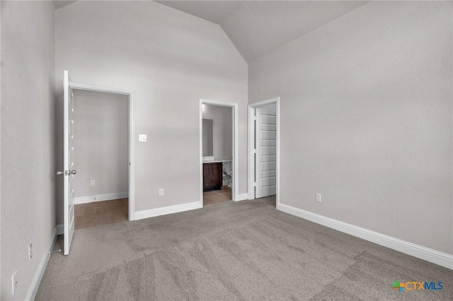 unfurnished bedroom with high vaulted ceiling, light colored carpet, and ensuite bath