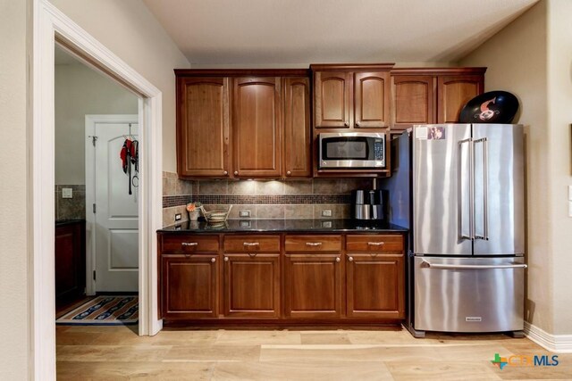 kitchen with decorative backsplash, light hardwood / wood-style floors, stainless steel appliances, and dark stone counters