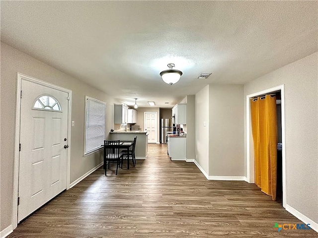 foyer entrance featuring baseboards, dark wood-style floors, a textured ceiling, and visible vents