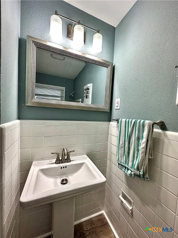bathroom featuring a textured wall, tile walls, wood finished floors, and a wainscoted wall