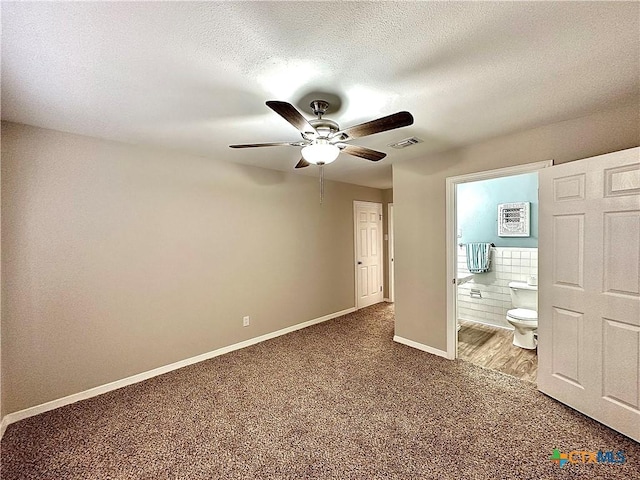unfurnished bedroom with a textured ceiling, visible vents, baseboards, carpet flooring, and ensuite bath