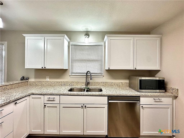 kitchen featuring white cabinets, stainless steel appliances, light stone countertops, and a sink