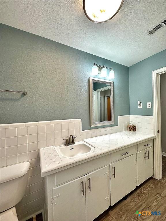 bathroom featuring visible vents, vanity, wood finished floors, toilet, and a textured ceiling