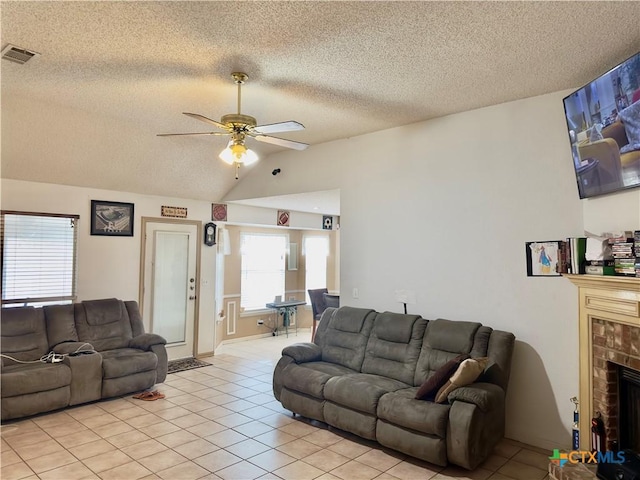 tiled living room with vaulted ceiling, ceiling fan, a fireplace, and a textured ceiling