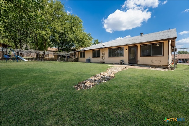 rear view of property with a playground, central air condition unit, and a yard