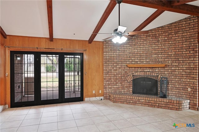 unfurnished living room featuring wood walls, a brick fireplace, lofted ceiling with beams, tile patterned floors, and a ceiling fan