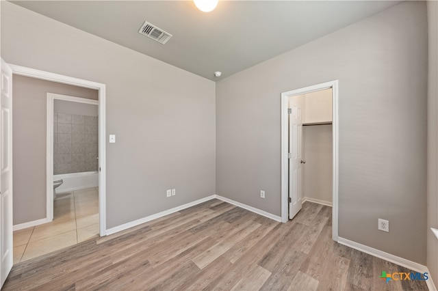 unfurnished bedroom featuring a closet, a spacious closet, connected bathroom, and light hardwood / wood-style flooring