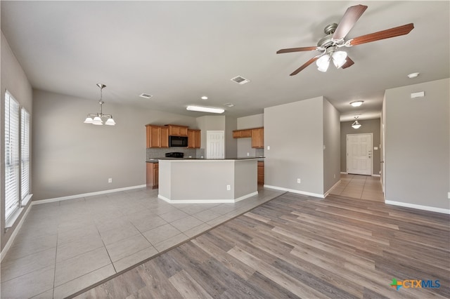 kitchen featuring backsplash, ceiling fan with notable chandelier, pendant lighting, light tile patterned floors, and a kitchen island