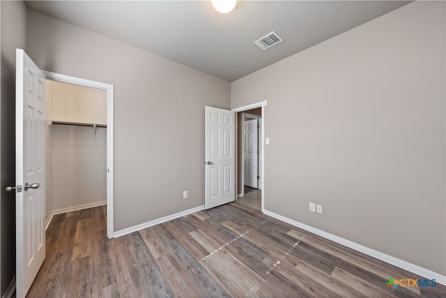 unfurnished bedroom featuring a walk in closet, dark wood-type flooring, and a closet