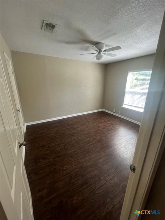 spare room with a textured ceiling, ceiling fan, and dark wood-type flooring