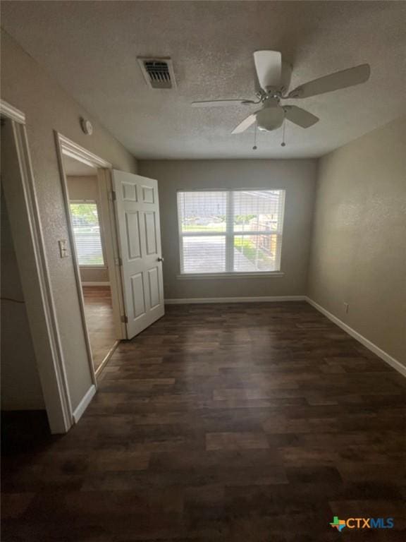 empty room featuring plenty of natural light, ceiling fan, and dark hardwood / wood-style flooring