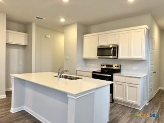 kitchen with sink, white cabinetry, appliances with stainless steel finishes, dark hardwood / wood-style flooring, and a kitchen island with sink